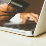 Hände mit Bankkarte vor einem aufgeklappten Laptop beim Online-Banking