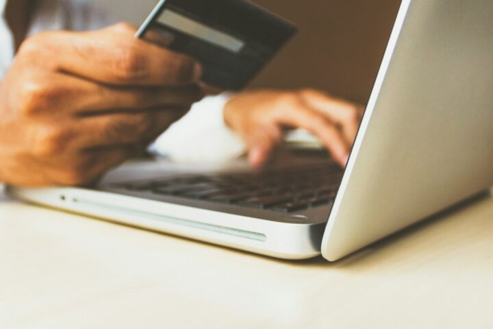 Hände mit Bankkarte vor einem aufgeklappten Laptop beim Online-Banking