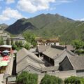 Traditionelle Gebäude am Fuß bewaldeter Berge mit Sicht auf die Chinesische Mauer am Hang