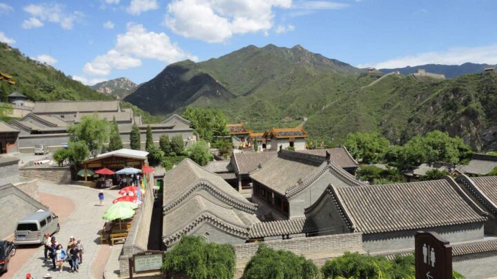 Traditionelle Gebäude am Fuß bewaldeter Berge mit Sicht auf die Chinesische Mauer am Hang