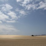 Helle Sanddünen auf Fuerteventura unter teilweise bewölktem Himmel mit Bergen am Horizont