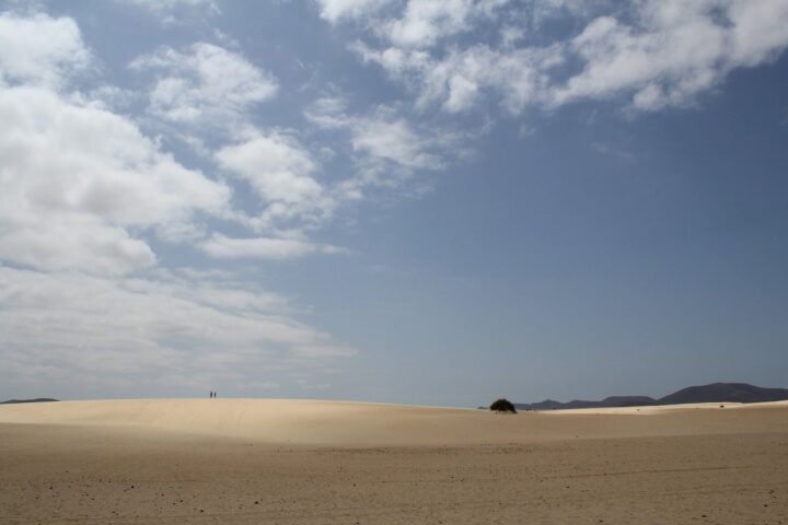 Helle Sanddünen auf Fuerteventura unter teilweise bewölktem Himmel mit Bergen am Horizont