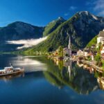 Ort Hallstatt am Hallstätter See mit Kirchturm, Boot und steilen Bergen unter blauem Himmel