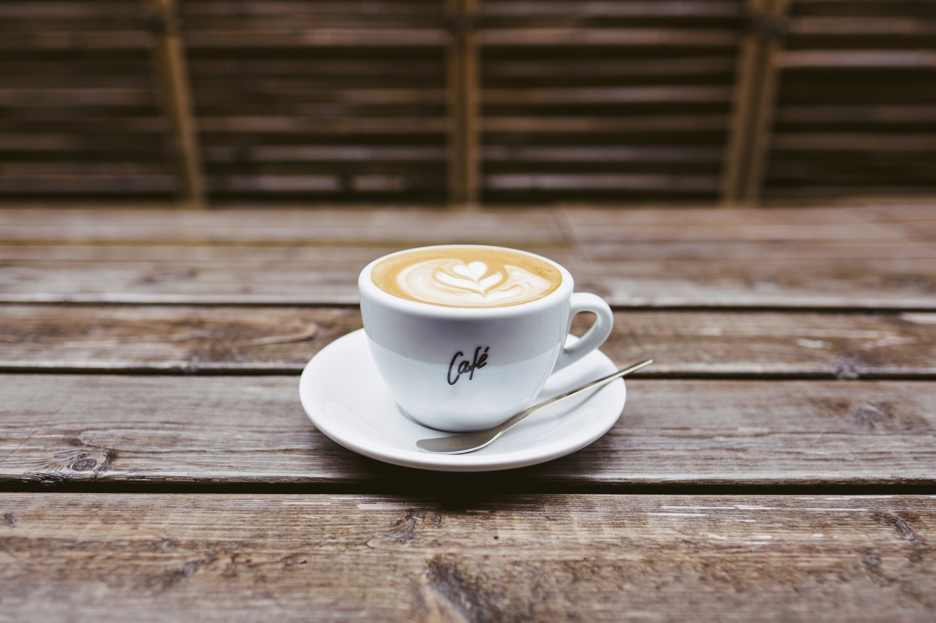 Weiße Kaffeetasse mit Latte-Art auf einer Untertasse auf einem Holztisch