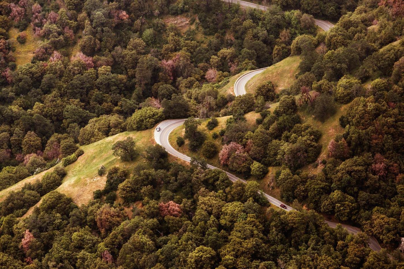 Luftbild einer kurvenreichen Asphaltstraße durch bewaldete Hügel und Berge