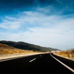 Leere mehrspurige Autobahn durch eine Hügellandschaft unter blauem Himmel
