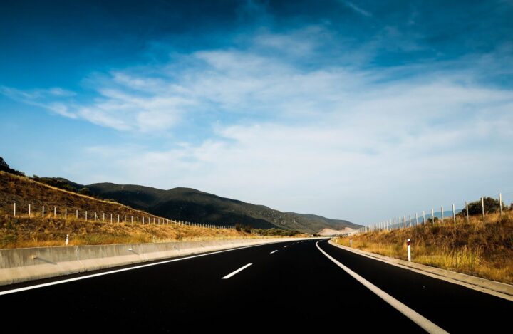 Leere mehrspurige Autobahn durch eine Hügellandschaft unter blauem Himmel