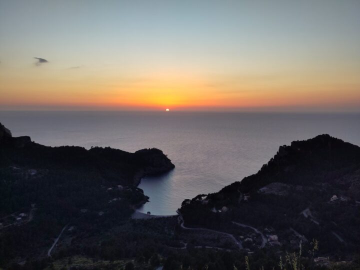 Sonnenuntergang über der Bucht Cala Tuent auf Mallorca zwischen dunklen Hügeln