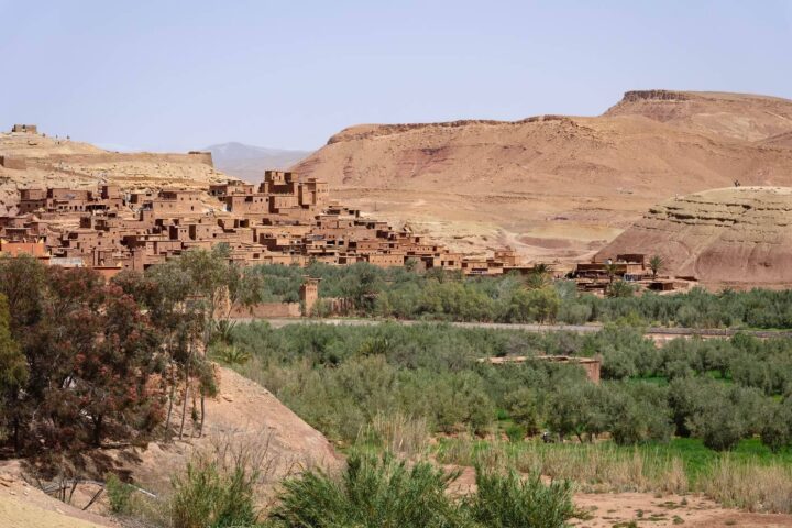 Lehmkasbah Aït Benhaddou in Marokko über einer grünen Oase vor karger Bergkulisse