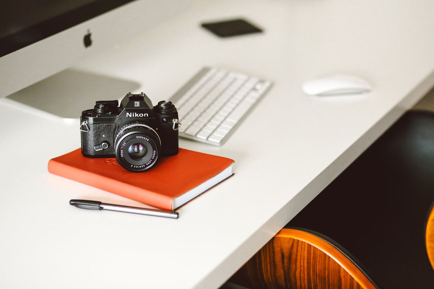 Schreibtisch mit Analogkamera auf orangem Notizbuch, Tastatur und Computermaus