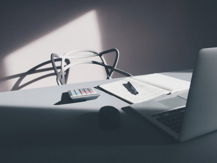 Heller Schreibtisch mit Laptop, Taschenrechner, Notizbuch und Maus im Sonnenlicht