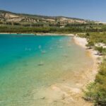 Andalusischer Stausee mit klarem türkisem Wasser, Kiesufer und Olivenhainen an den Hängen