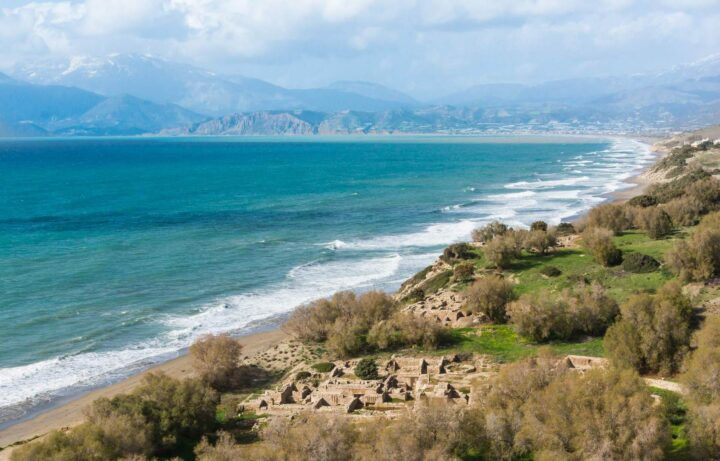 Mittelmeerküste mit antiken Ruinen auf einem Gras hang und türkisem Meer vor Bergkulisse
